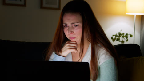 Anxious-Woman-Sitting-On-Sofa-At-Home-At-Night-Looking-At-Laptop-Concerned-About-Social-Media-Or-Bad-News-1